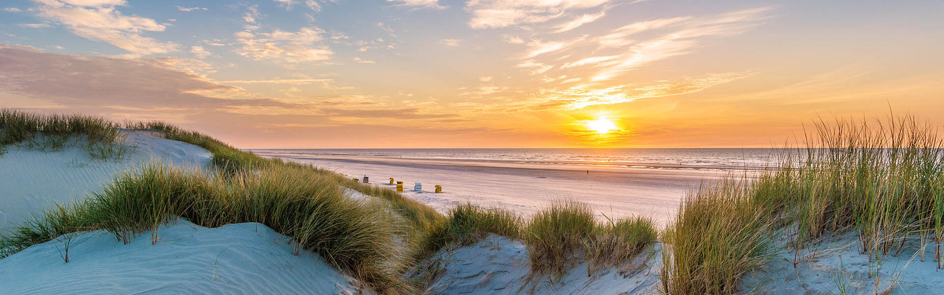 Ansicht eines Sonnenuntergangs am Strand mit Sanddünen und im Hintergrund sind Strandkörbe