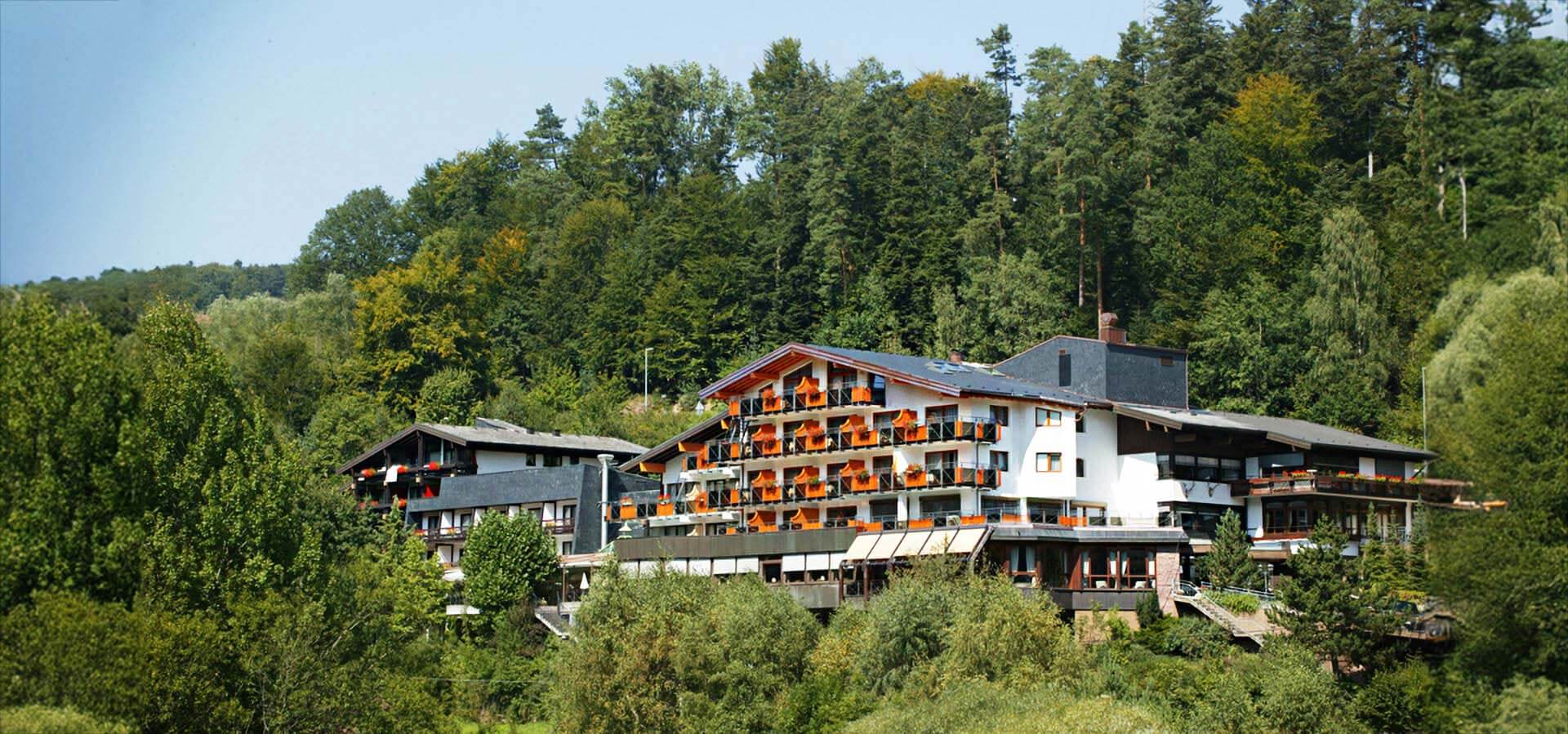 Außenansicht auf das Mönchs Waldhotel mit Tannen- und Laubbäumen darum herum